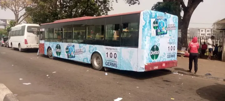 Red and white city bus with a full wrap, parked beside a busy street