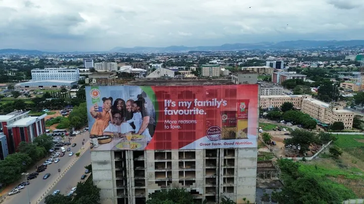 Wide aerial of the Golden Penny wall drape on the PDP Building with the Abuja skyline behind, for FMN