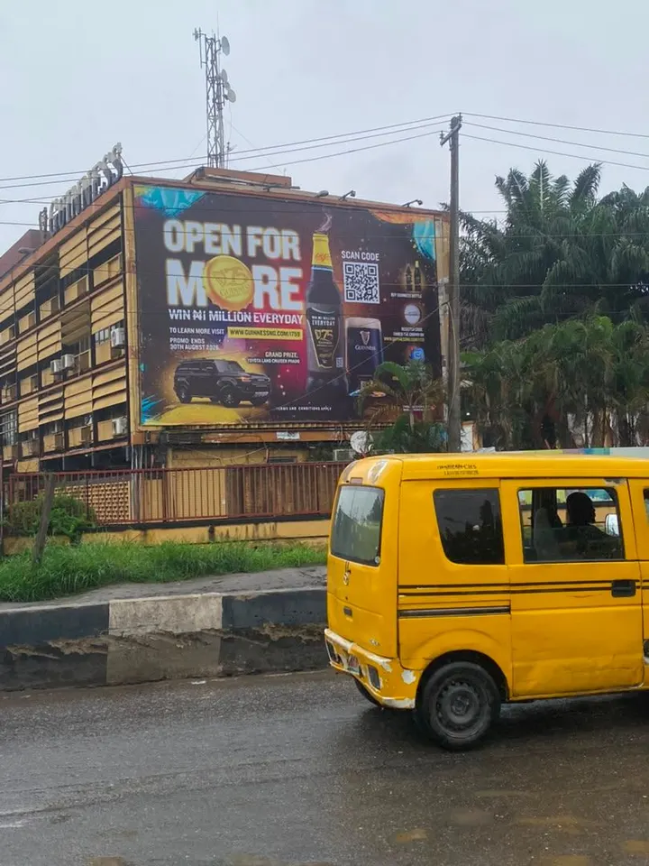 Guinness Open for More wall drape on a building in Lagos, with a danfo passing